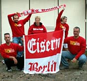Fünf junge Frauen und Männer posieren für ein Foto mit Eisern Union Poster, Schal und T-Shirts